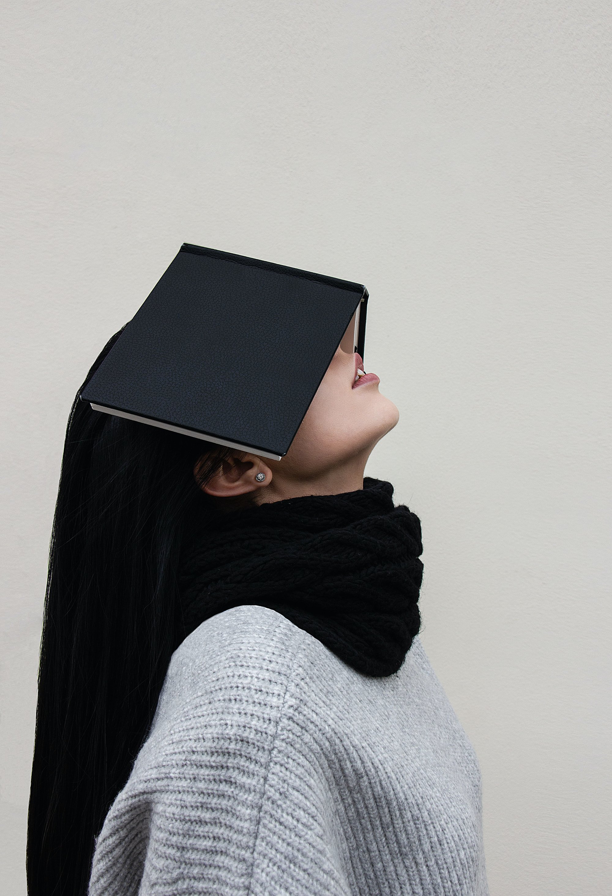 Frau mit grauem Pulli, die ihre Augen mit einem schwarzen Buch bedeckt
Foto: Valerie Lendel